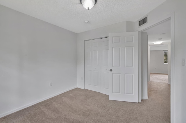 unfurnished bedroom featuring visible vents, a closet, baseboards, a textured ceiling, and carpet flooring