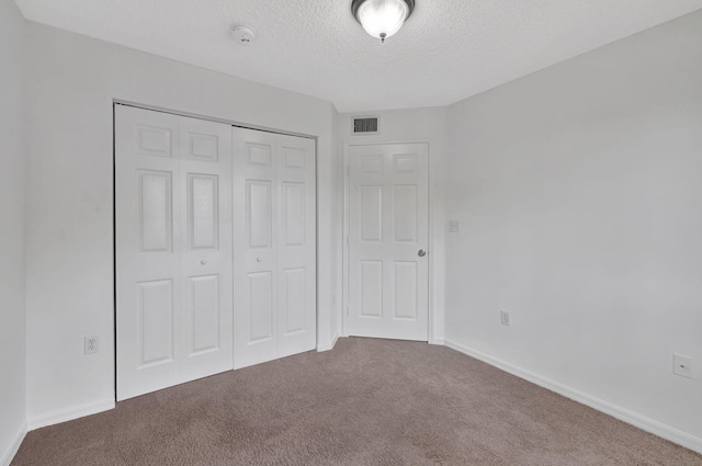 unfurnished bedroom with a textured ceiling, visible vents, carpet floors, baseboards, and a closet