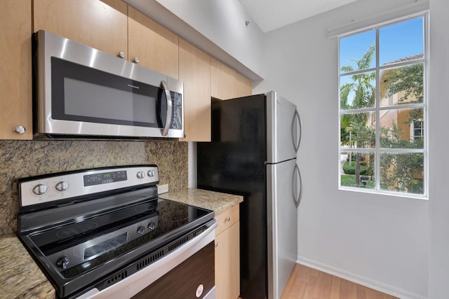 kitchen featuring light brown cabinetry, appliances with stainless steel finishes, light wood finished floors, baseboards, and backsplash