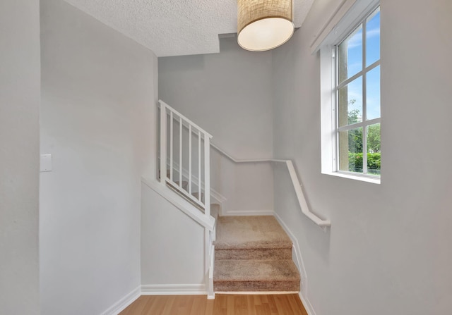 stairs featuring a textured ceiling, baseboards, wood finished floors, and a wealth of natural light