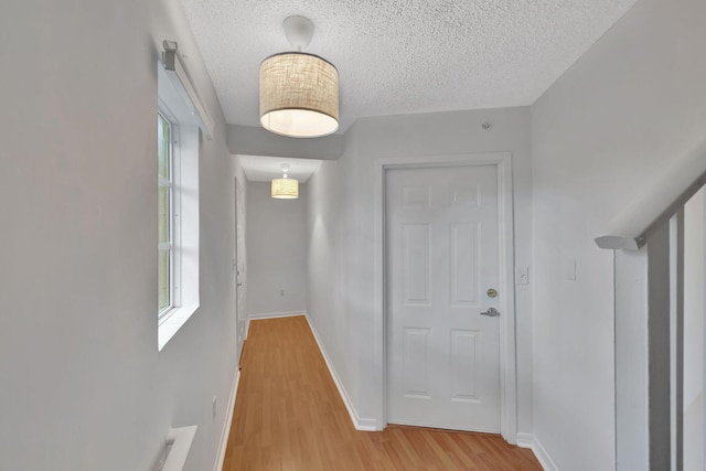 hallway featuring plenty of natural light, a textured ceiling, light wood-style flooring, and baseboards