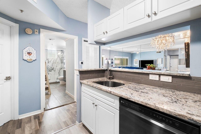 kitchen featuring tasteful backsplash, light stone counters, dishwashing machine, sink, and white cabinets