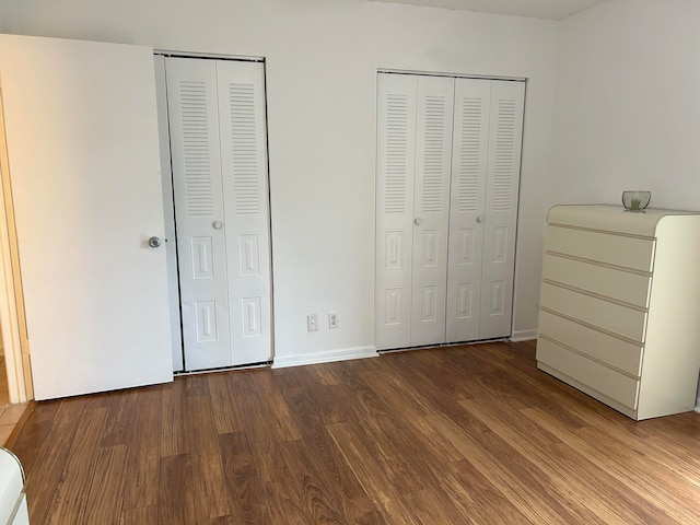 unfurnished bedroom with wood-type flooring and multiple closets