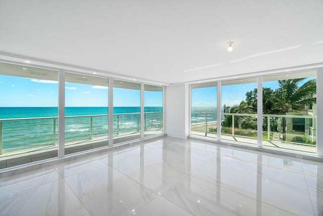 unfurnished room featuring floor to ceiling windows, a water view, and a view of the beach