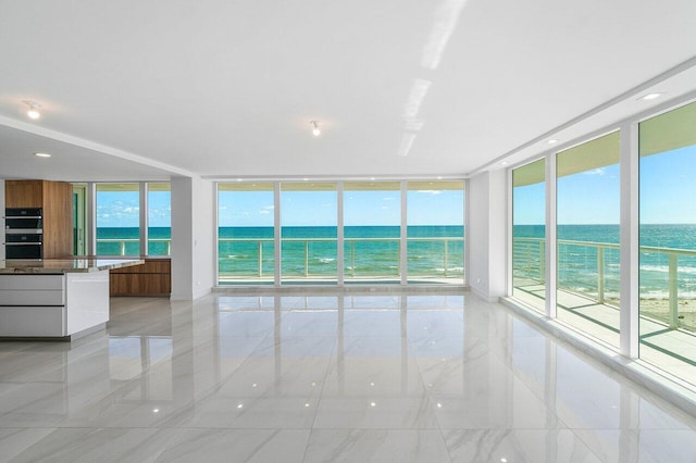 spare room with a water view, a wall of windows, a healthy amount of sunlight, and a view of the beach