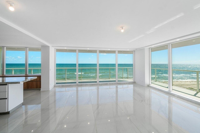 spare room with expansive windows, a water view, and a view of the beach