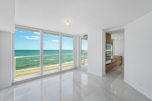 empty room featuring floor to ceiling windows, a beach view, and a water view