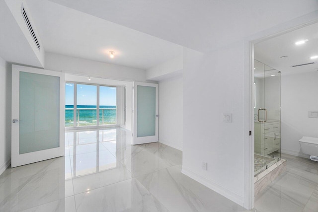 interior space featuring visible vents, a water view, marble finish floor, a shower stall, and baseboards