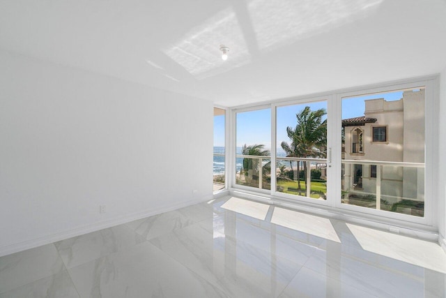 unfurnished room with baseboards, marble finish floor, floor to ceiling windows, and a water view