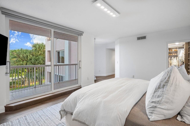 bedroom with hardwood / wood-style floors, multiple windows, and a walk in closet