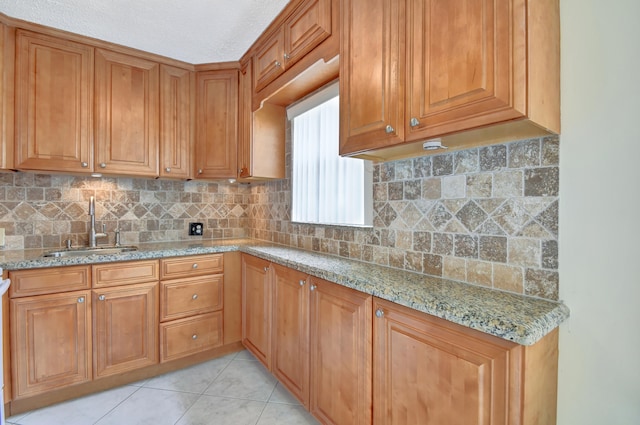 kitchen featuring tasteful backsplash, a textured ceiling, light stone countertops, light tile patterned flooring, and sink