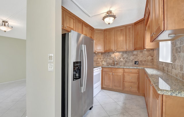 kitchen with decorative backsplash, stainless steel fridge, sink, light stone counters, and white range