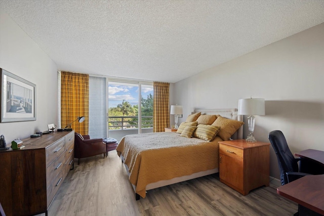 bedroom featuring a wall of windows, dark hardwood / wood-style floors, and a textured ceiling