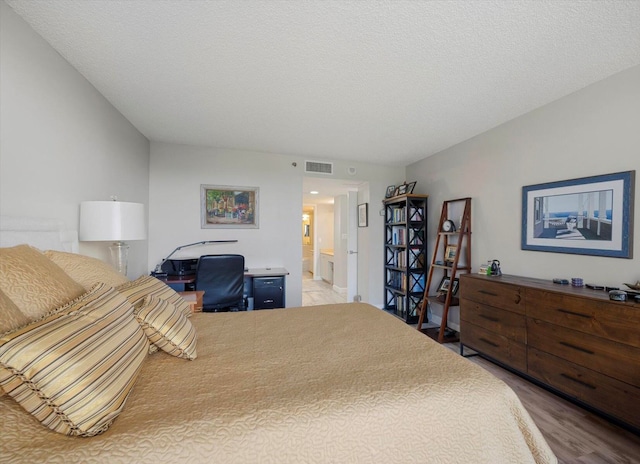 bedroom featuring wood-type flooring, a textured ceiling, and ensuite bath