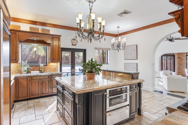 kitchen with a center island, french doors, ceiling fan with notable chandelier, tasteful backsplash, and light stone counters