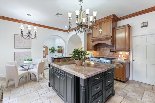 kitchen with light stone counters, backsplash, crown molding, a chandelier, and a kitchen island