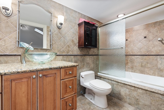 full bathroom with tile patterned floors, vanity, bath / shower combo with glass door, and tile walls