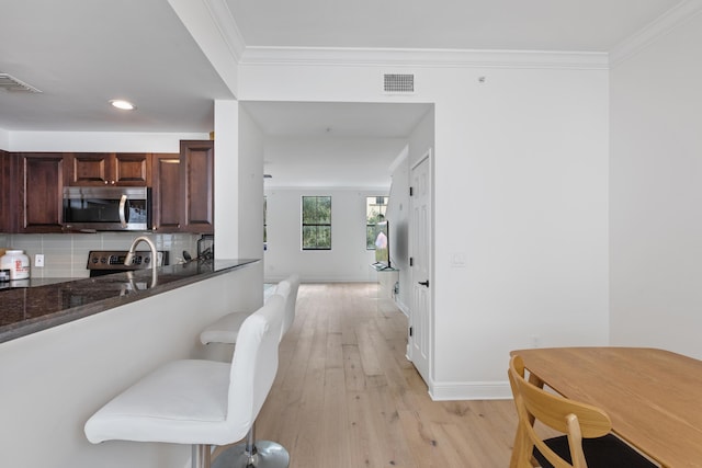 kitchen featuring light hardwood / wood-style flooring, tasteful backsplash, dark stone countertops, crown molding, and kitchen peninsula