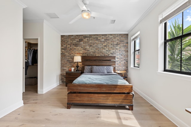 bedroom with light hardwood / wood-style flooring, a walk in closet, brick wall, and ornamental molding