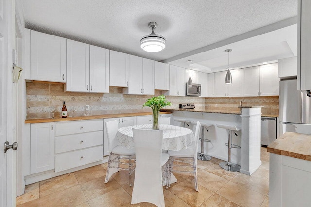 kitchen featuring a kitchen breakfast bar, stainless steel appliances, wood counters, a center island, and white cabinetry