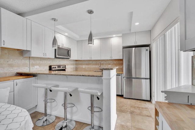 kitchen featuring white cabinetry, stainless steel appliances, hanging light fixtures, and a kitchen bar