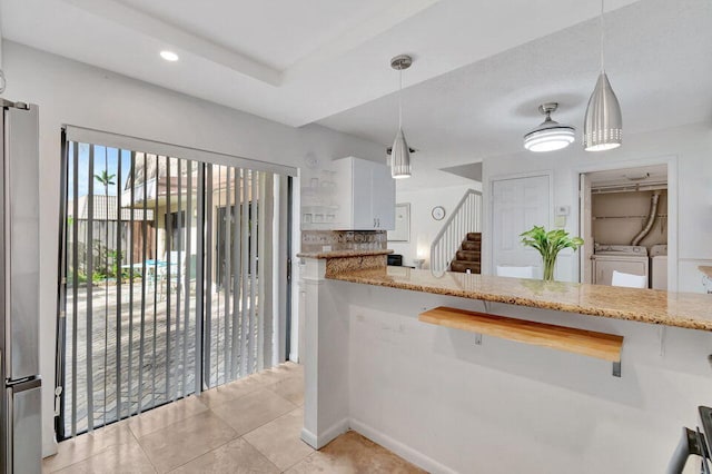 kitchen with hanging light fixtures, white cabinetry, light stone countertops, stainless steel refrigerator, and washing machine and dryer