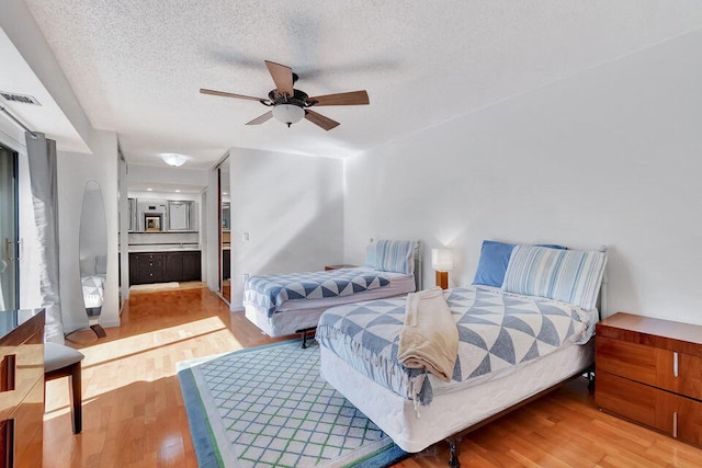 bedroom featuring connected bathroom, ceiling fan, a textured ceiling, and light hardwood / wood-style flooring