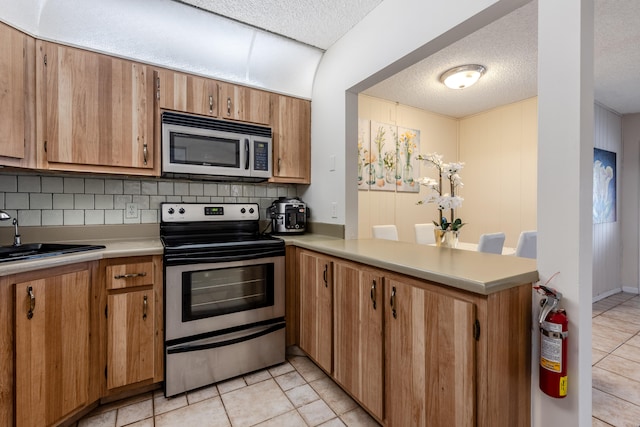 kitchen featuring light tile patterned floors, sink, kitchen peninsula, appliances with stainless steel finishes, and decorative backsplash