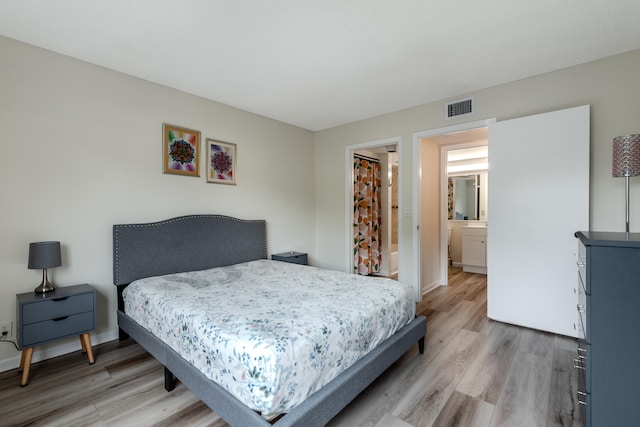 bedroom with connected bathroom and light hardwood / wood-style floors