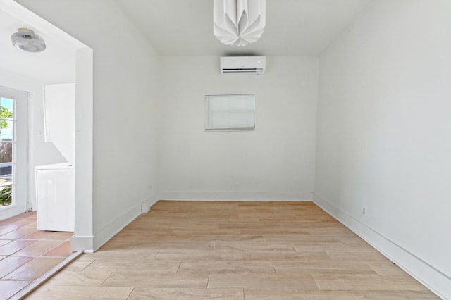 unfurnished room featuring washer / dryer, a wall mounted AC, light hardwood / wood-style floors, and a healthy amount of sunlight