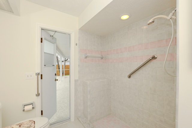 bathroom featuring a textured ceiling, toilet, and a tile shower