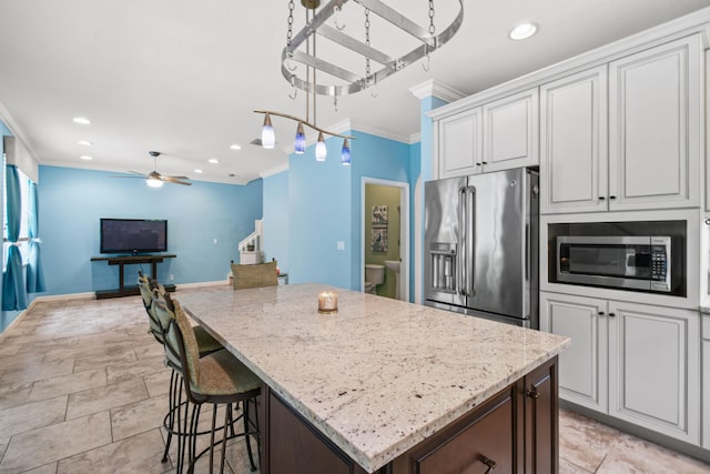 kitchen with white cabinets, a kitchen island, appliances with stainless steel finishes, light stone countertops, and crown molding