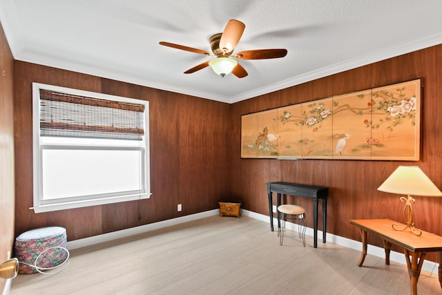 misc room featuring light hardwood / wood-style floors, crown molding, wooden walls, and ceiling fan