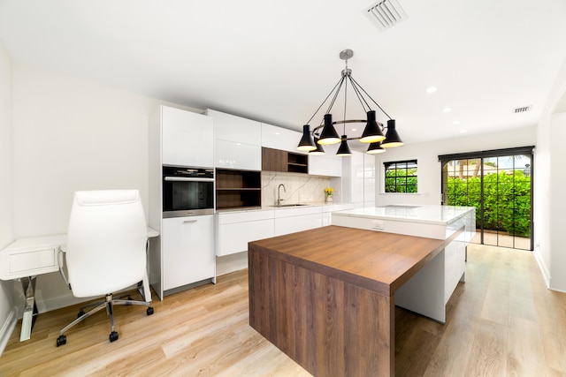 kitchen featuring a kitchen island, stainless steel oven, sink, hanging light fixtures, and white cabinetry