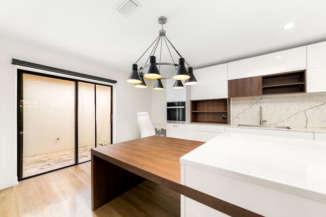 kitchen with light hardwood / wood-style flooring, stainless steel oven, decorative light fixtures, sink, and white cabinets