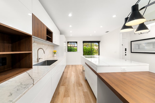 kitchen featuring light stone counters, hanging light fixtures, sink, white cabinetry, and light wood-type flooring