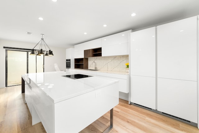 kitchen with pendant lighting, white cabinets, a kitchen island, black electric stovetop, and light hardwood / wood-style floors