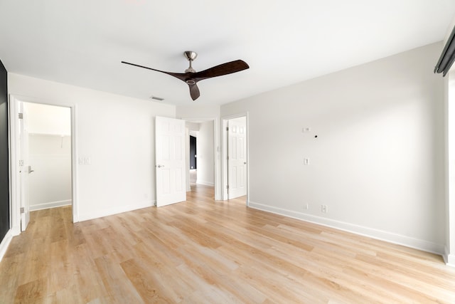 unfurnished bedroom with a closet, a walk in closet, light hardwood / wood-style flooring, and ceiling fan