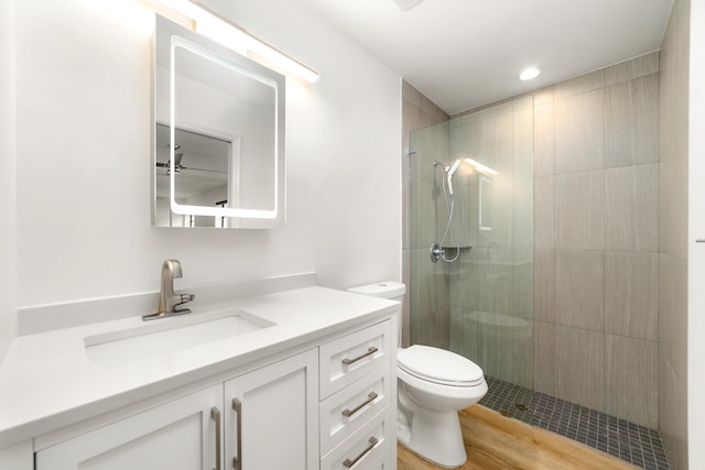 bathroom with hardwood / wood-style floors, a tile shower, vanity, and toilet