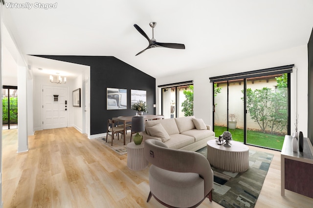 living room featuring ceiling fan with notable chandelier, light hardwood / wood-style floors, and vaulted ceiling