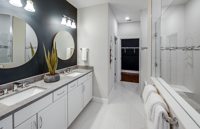 full bath featuring double vanity, baseboards, a tile shower, and a sink