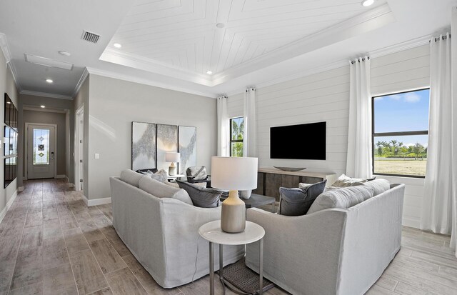 living room featuring baseboards, visible vents, a raised ceiling, ornamental molding, and light wood-style floors