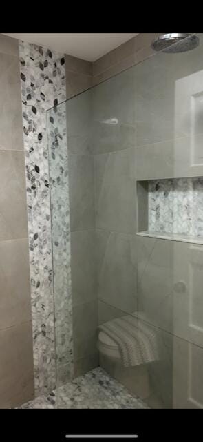 bathroom featuring tiled shower and toilet