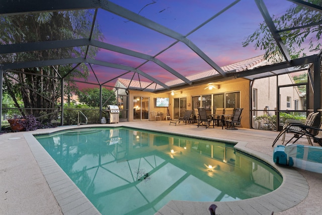 pool at dusk with area for grilling, glass enclosure, and a patio