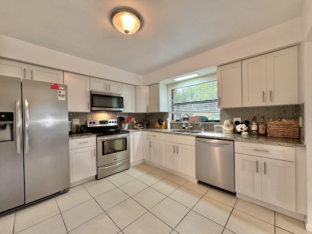 kitchen with light tile patterned flooring, dark stone counters, a sink, backsplash, and stainless steel appliances