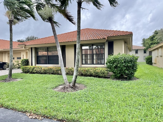 view of front of home featuring a tiled roof, a front yard, and stucco siding