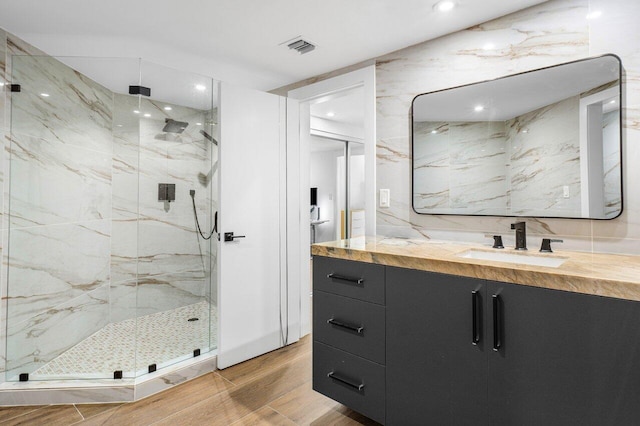 bathroom with tile walls, vanity, wood-type flooring, and a shower with shower door