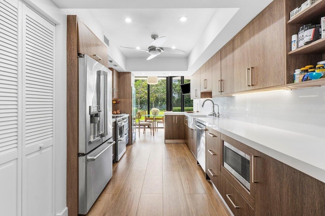 kitchen with stainless steel appliances, light hardwood / wood-style floors, ceiling fan, and sink