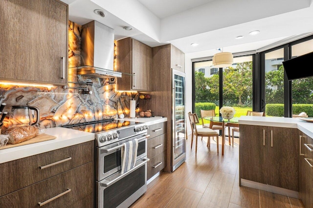 kitchen with range with two ovens, wall chimney range hood, backsplash, pendant lighting, and light wood-type flooring