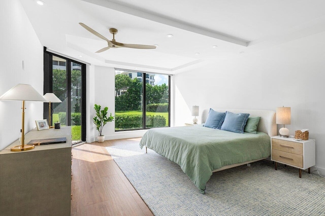 bedroom featuring expansive windows, light hardwood / wood-style flooring, ceiling fan, and a tray ceiling